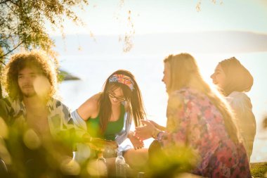 Bir grup arkadaş plajda toplanıp müzik, kahkaha ve birlikteliğin sıcaklığıyla dolu neşeli anları paylaşıyorlar. Gençler sahilde eğleniyor.