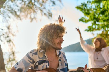Bir grup arkadaş plajda toplanıp müzik, kahkaha ve birlikteliğin sıcaklığıyla dolu neşeli anları paylaşıyorlar. Gençler sahilde eğleniyor.