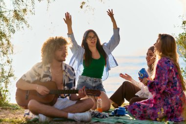 Bir grup arkadaş plajda toplanıp müzik, kahkaha ve birlikteliğin sıcaklığıyla dolu neşeli anları paylaşıyorlar. Gençler sahilde eğleniyor.
