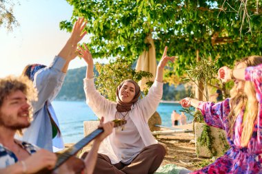 Bir grup arkadaş plajda toplanıp müzik, kahkaha ve birlikteliğin sıcaklığıyla dolu neşeli anları paylaşıyorlar. Gençler sahilde eğleniyor.