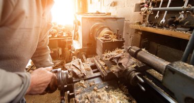 Aletler, ahşap kalıplar ve endüstriyel ekipmanlarla dolu kırsal ve dağınık bir atölyede makinelerle çalışan yaşlı bir zanaatkar. Sıcak güneş ışığı sahneye nostaljik ve klasik bir his katıyor.