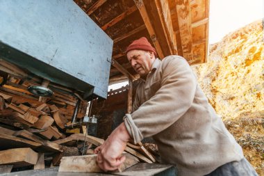 Bir marangoz elinin, kaba ahşap bir kalası, kırsal bir atölyedeki testerenin içinden geçirdiği yakın çekim. Görüntü, marangozluk, hassasiyet ve ahşap işçiliğindeki sıkı çalışmayı yakalıyor.
