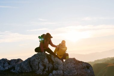 İki yürüyüşçü, açık hava ekipmanlı çift güneş doğarken kayalık araziye tırmanır. Dağcılar gün doğumunda dağın zirvesine ulaşır.