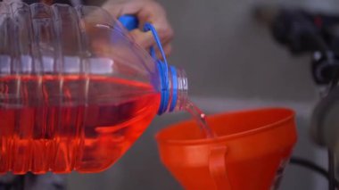 Plastik şişe ve huni kullanarak motorsiklet yakıt deposuna benzin döken bir adamın yakın plan fotoğrafı.
