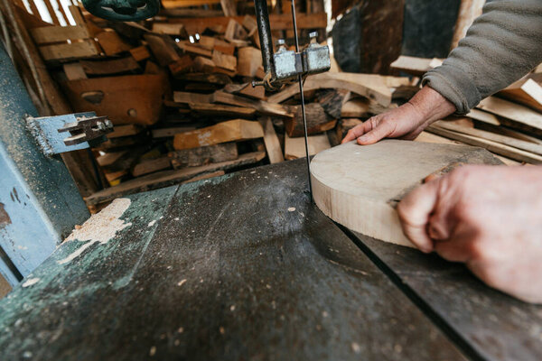 A close up shot of a carpenters hands guiding a rough wooden plank through a bandsaw in a rustic workshop. The image captures the craftsmanship, precision, and hard work involved in woodworking, with