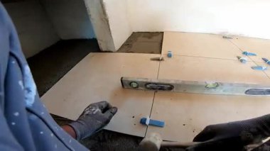 Seramik döşeme döşemesi takan profesyonel bir klasörün POV görüntüsü. Video, fayans yapıştırıcı sürme, fayansları yerleştirme ve onları zemine sabitlemek için bir çekiç kullanma sürecini kaydediyor. İdeal