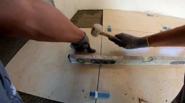 Seramik döşeme döşemesi takan profesyonel bir klasörün POV görüntüsü. Video, fayans yapıştırıcı sürme, fayansları yerleştirme ve onları zemine sabitlemek için bir çekiç kullanma sürecini kaydediyor. İdeal