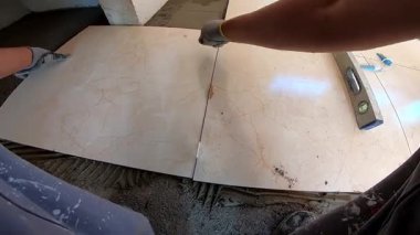 Seramik döşeme döşemesi takan profesyonel bir klasörün POV görüntüsü. Video, fayans yapıştırıcı sürme, fayansları yerleştirme ve onları zemine sabitlemek için bir çekiç kullanma sürecini kaydediyor. İdeal