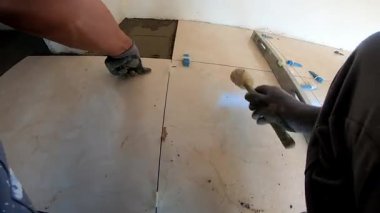 Seramik döşeme döşemesi takan profesyonel bir klasörün POV görüntüsü. Video, fayans yapıştırıcı sürme, fayansları yerleştirme ve onları zemine sabitlemek için bir çekiç kullanma sürecini kaydediyor. İdeal