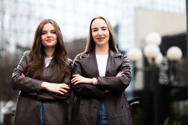 Deri ceketli iki kendine güvenen genç kadın şehir ortamında kollarını kavuşturmuş poz veriyorlar. Güçlendirme ve modern kadın yaşam tarzı.