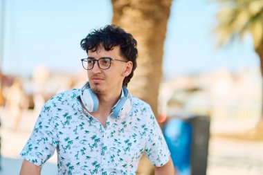 Gözlük ve kulaklık takan neşeli genç bir adam sıcak, güneşli bir açık havada ışıl ışıl gülümsüyor, kendine güven ve pozitiflik saçıyor.. 