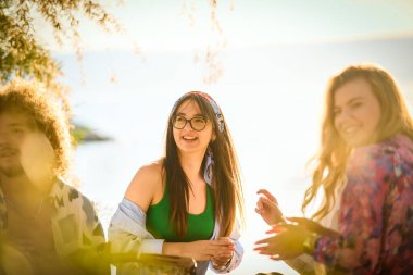 Bir grup arkadaş plajda toplanıp müzik, kahkaha ve birlikteliğin sıcaklığıyla dolu neşeli anları paylaşıyorlar. Gençler sahilde eğleniyor.