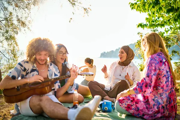 Bir grup arkadaş plajda toplanıp müzik, kahkaha ve birlikteliğin sıcaklığıyla dolu neşeli anları paylaşıyorlar. Gençler sahilde eğleniyor.