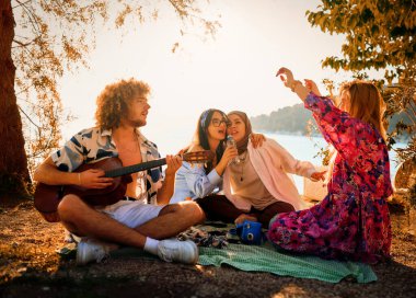 Bir grup arkadaş plajda toplanıp müzik, kahkaha ve birlikteliğin sıcaklığıyla dolu neşeli anları paylaşıyorlar. Gençler sahilde eğleniyor.