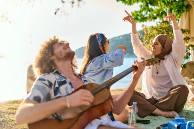 Bir grup arkadaş plajda toplanıp müzik, kahkaha ve birlikteliğin sıcaklığıyla dolu neşeli anları paylaşıyorlar. Gençler sahilde eğleniyor.
