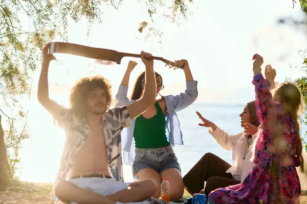 Bir grup arkadaş plajda toplanıp müzik, kahkaha ve birlikteliğin sıcaklığıyla dolu neşeli anları paylaşıyorlar. Gençler sahilde eğleniyor.