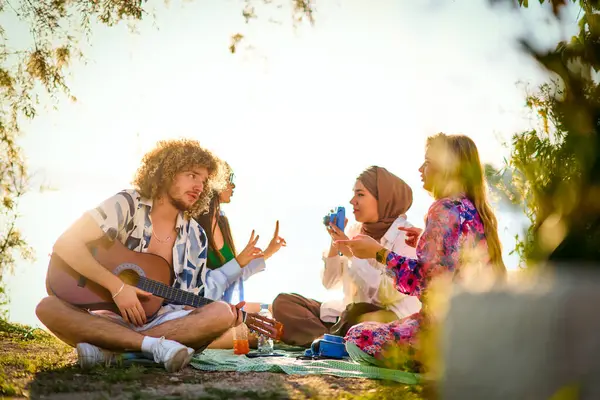 Bir grup arkadaş plajda toplanıp müzik, kahkaha ve birlikteliğin sıcaklığıyla dolu neşeli anları paylaşıyorlar. Gençler sahilde eğleniyor.