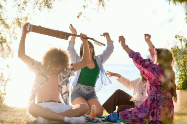 Bir grup arkadaş plajda toplanıp müzik, kahkaha ve birlikteliğin sıcaklığıyla dolu neşeli anları paylaşıyorlar. Gençler sahilde eğleniyor.