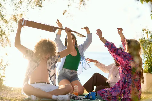 Bir grup arkadaş plajda toplanıp müzik, kahkaha ve birlikteliğin sıcaklığıyla dolu neşeli anları paylaşıyorlar. Gençler sahilde eğleniyor.