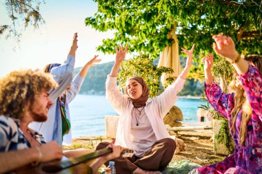 Bir grup arkadaş plajda toplanıp müzik, kahkaha ve birlikteliğin sıcaklığıyla dolu neşeli anları paylaşıyorlar. Gençler sahilde eğleniyor.