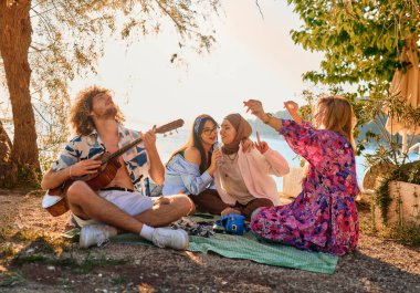 Bir grup arkadaş plajda toplanıp müzik, kahkaha ve birlikteliğin sıcaklığıyla dolu neşeli anları paylaşıyorlar. Gençler sahilde eğleniyor.