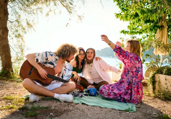Bir grup arkadaş plajda toplanıp müzik, kahkaha ve birlikteliğin sıcaklığıyla dolu neşeli anları paylaşıyorlar. Gençler sahilde eğleniyor.