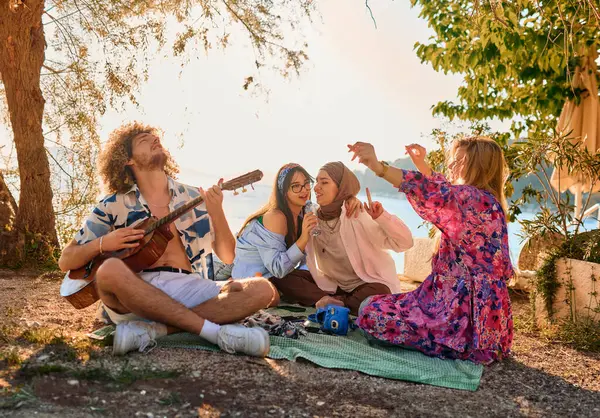 Bir grup arkadaş plajda toplanıp müzik, kahkaha ve birlikteliğin sıcaklığıyla dolu neşeli anları paylaşıyorlar. Gençler sahilde eğleniyor.