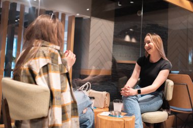 İki genç kadın yan yana oturmuş modern bir kahve dükkanında sohbet ederken gülüyorlar..