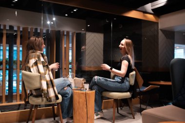 İki genç kadın yan yana oturmuş modern bir kahve dükkanında sohbet ederken gülüyorlar..