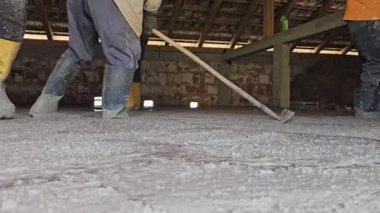 Hakiki hayat insanları sarı çizmeli işçiler inşaat alanındaki tırmıkları kullanarak yeni dökülmüş betonu dümdüz ediyorlar. Düşük açıyla ateş edilmiş, takım çalışmasını ve el işçiliğini gösteriyor