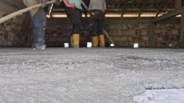 Hakiki hayat insanları sarı çizmeli işçiler inşaat alanındaki tırmıkları kullanarak yeni dökülmüş betonu dümdüz ediyorlar. Düşük açıyla ateş edilmiş, takım çalışmasını ve el işçiliğini gösteriyor