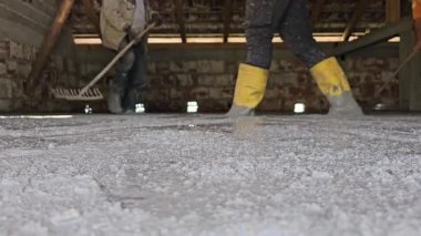 Hakiki hayat insanları sarı çizmeli işçiler inşaat alanındaki tırmıkları kullanarak yeni dökülmüş betonu dümdüz ediyorlar. Düşük açıyla ateş edilmiş, takım çalışmasını ve el işçiliğini gösteriyor