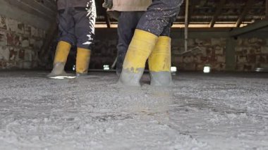 Hakiki hayat insanları sarı çizmeli işçiler inşaat alanındaki tırmıkları kullanarak yeni dökülmüş betonu dümdüz ediyorlar. Düşük açıyla ateş edilmiş, takım çalışmasını ve el işçiliğini gösteriyor