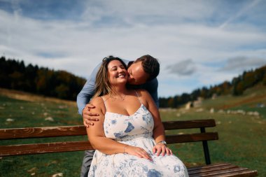 Erkek, dışarıda otururken partnerinin omzunu öper. Sevgisini, neşesini ve duygusal bağını gösterir..