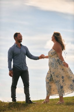 Çimenli bir dağ tarlasında neşeli bir şekilde dans eden erkek ve kadın aydınlık bir günde, doğada sevgi ve özgürlüğün tadını çıkarıyorlar..