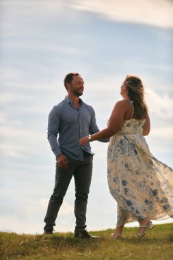 Çimenli bir dağ tarlasında neşeli bir şekilde dans eden erkek ve kadın aydınlık bir günde, doğada sevgi ve özgürlüğün tadını çıkarıyorlar..