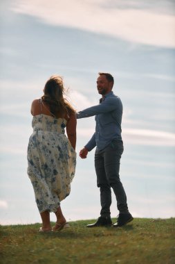 Çimenli bir dağ tarlasında neşeli bir şekilde dans eden erkek ve kadın aydınlık bir günde, doğada sevgi ve özgürlüğün tadını çıkarıyorlar..