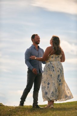 Çimenli bir dağ tarlasında neşeli bir şekilde dans eden erkek ve kadın aydınlık bir günde, doğada sevgi ve özgürlüğün tadını çıkarıyorlar..