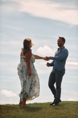 Çimenli bir dağ tarlasında neşeli bir şekilde dans eden erkek ve kadın aydınlık bir günde, doğada sevgi ve özgürlüğün tadını çıkarıyorlar..