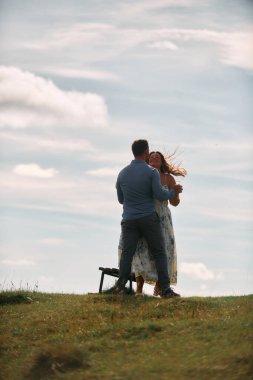 Çimenli bir dağ tarlasında neşeli bir şekilde dans eden erkek ve kadın aydınlık bir günde, doğada sevgi ve özgürlüğün tadını çıkarıyorlar..