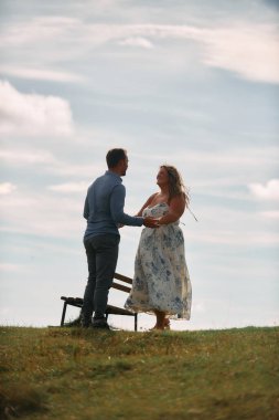 Çimenli bir dağ tarlasında neşeli bir şekilde dans eden erkek ve kadın aydınlık bir günde, doğada sevgi ve özgürlüğün tadını çıkarıyorlar..