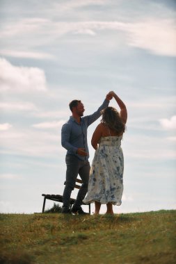 Çimenli bir dağ tarlasında neşeli bir şekilde dans eden erkek ve kadın aydınlık bir günde, doğada sevgi ve özgürlüğün tadını çıkarıyorlar..