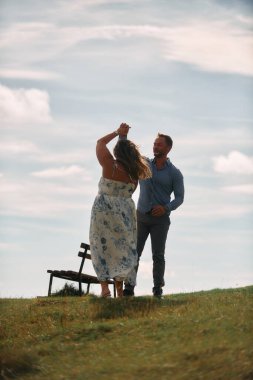 Çimenli bir dağ tarlasında neşeli bir şekilde dans eden erkek ve kadın aydınlık bir günde, doğada sevgi ve özgürlüğün tadını çıkarıyorlar..