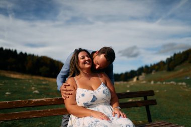 Erkek, dışarıda otururken partnerinin omzunu öper. Sevgisini, neşesini ve duygusal bağını gösterir..