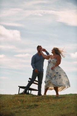 Çimenli bir dağ tarlasında neşeli bir şekilde dans eden erkek ve kadın aydınlık bir günde, doğada sevgi ve özgürlüğün tadını çıkarıyorlar..