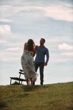 Çimenli bir dağ tarlasında neşeli bir şekilde dans eden erkek ve kadın aydınlık bir günde, doğada sevgi ve özgürlüğün tadını çıkarıyorlar..