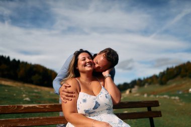Erkek, dışarıda otururken partnerinin omzunu öper. Sevgisini, neşesini ve duygusal bağını gösterir..
