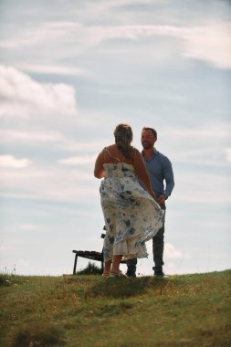Çimenli bir dağ tarlasında neşeli bir şekilde dans eden erkek ve kadın aydınlık bir günde, doğada sevgi ve özgürlüğün tadını çıkarıyorlar..