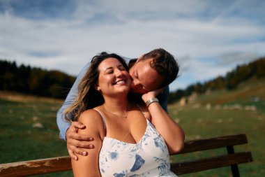 Erkek, dışarıda otururken partnerinin omzunu öper. Sevgisini, neşesini ve duygusal bağını gösterir..