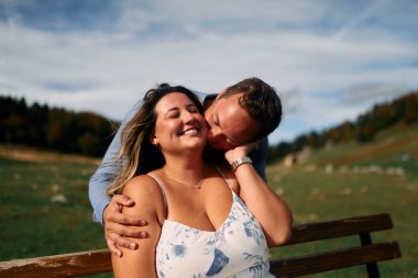 Erkek, dışarıda otururken partnerinin omzunu öper. Sevgisini, neşesini ve duygusal bağını gösterir..